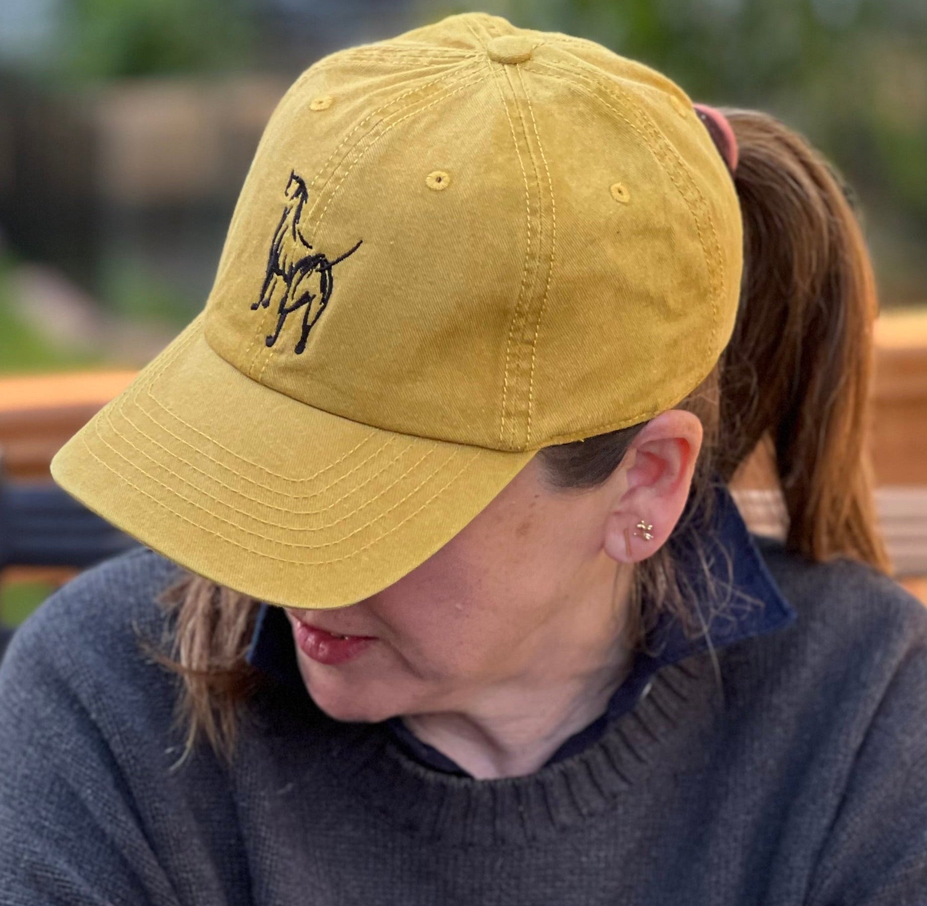 Person wearing a yellow cap with a logo, sitting outdoors on a wooden deck.