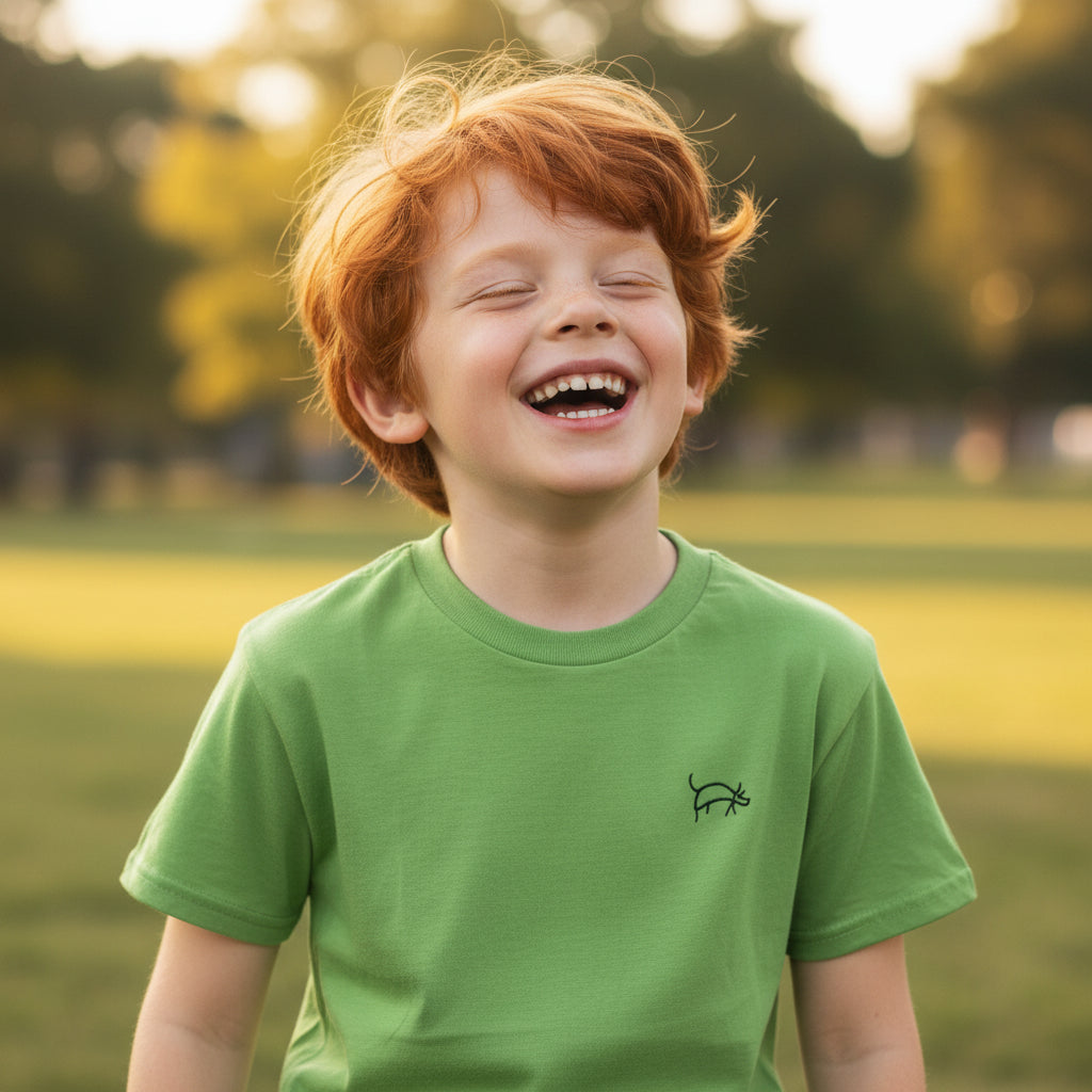 Child wearing a green t-shirt with a small logo, standing in a park.